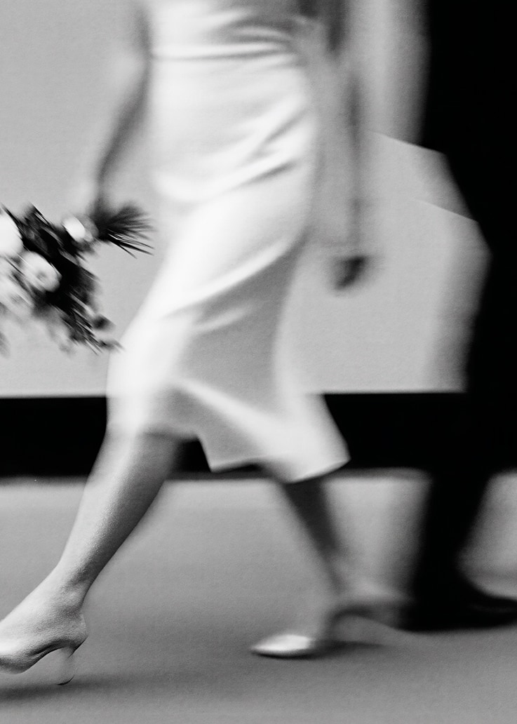 Foto en blanco y negro de una persona de vestido con flores caminando junto a otra persona.
