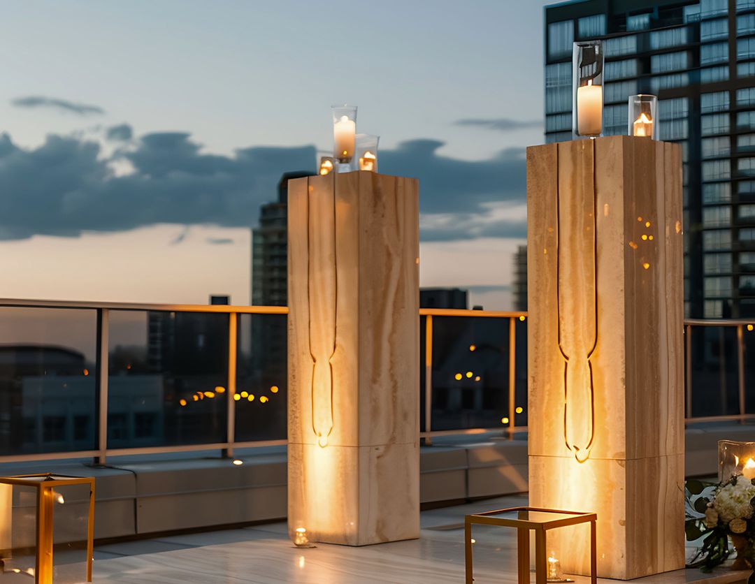 Terraza en altura al atardecer con dos columnas de madera iluminadas y la ciudad de fondo.