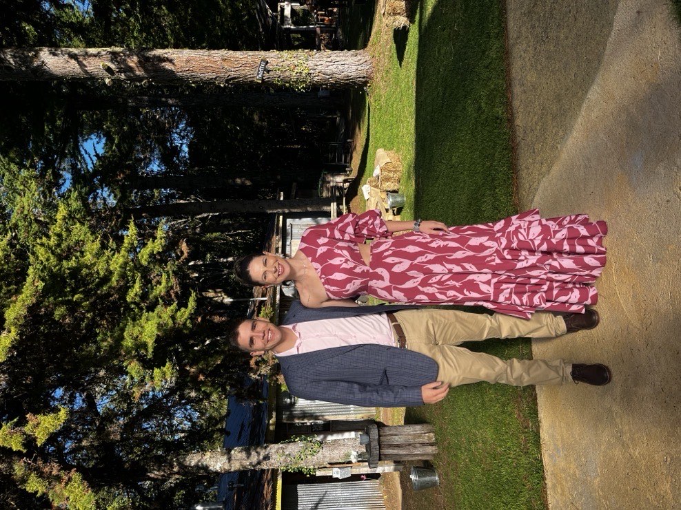 Stefy y Joaco sonriendo en un jardin, ella con vestido floreado rosa y el con chaleco y camisa