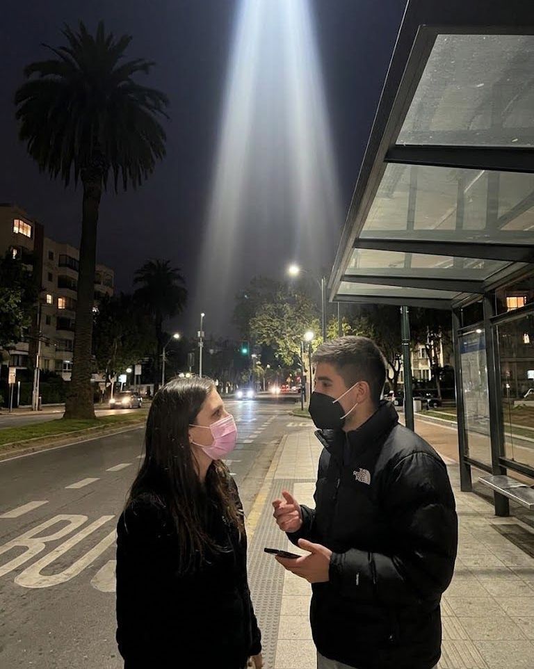 Stefy y Joaco conversando con mascarilla en un paradero de micros de noche