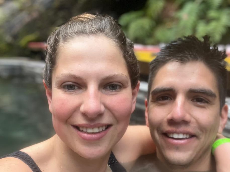 Stefy y Joaco sonriendo dentro de unas termas rodeadas de vegetación