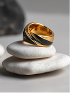 Anillo dorado y negro con dibujo, apoyado sobre piedras blancas apiladas.